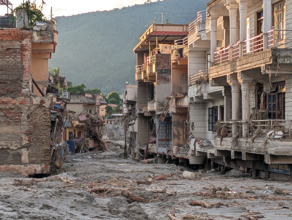 A street in a mountain valley in Nepal, with flood-damaged buildings on both sides and mud and debris covering the road