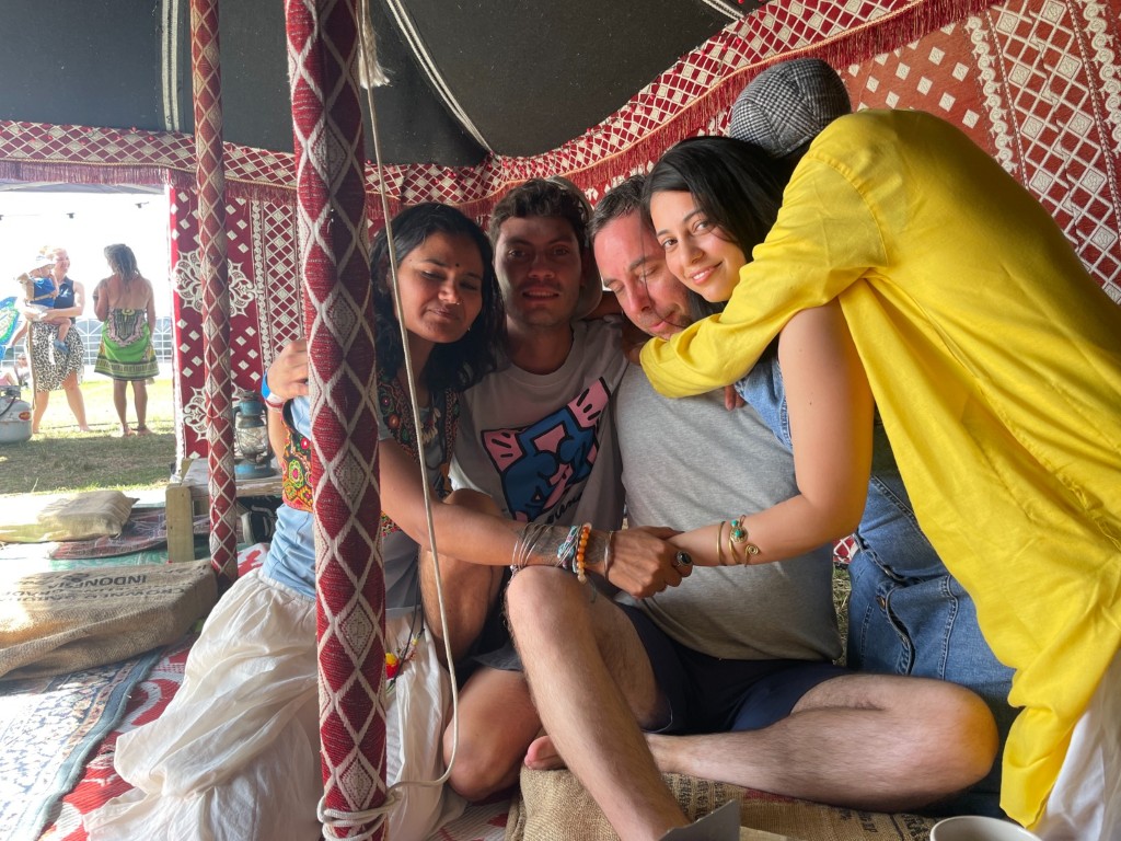 Dejan sitting with friends from Auckland’s yoga community, sharing a group hug inside a red patterned tent